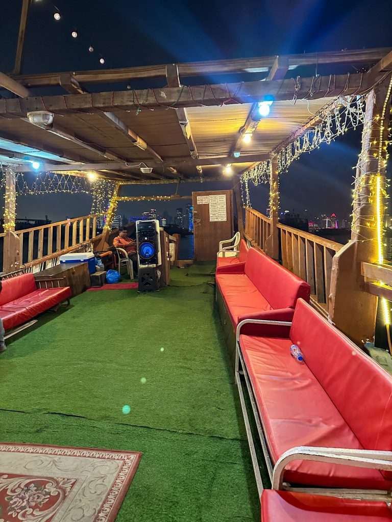 Onboard a traditional dhow at the end of a sunset dhow cruise. Red benches line each side of the boat with a grass green carpet lining the deck.